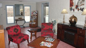 A living room with two red floral armchairs, a coffee table with magazines, a fireplace, and a bookshelf with postcards. - Red Carpet Inn - Louisville (Louisville)