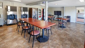 A spacious room with a long wooden table and chairs, a refrigerator, a vending machine, and a television. - Red Carpet Inn - Louisville (Louisville)