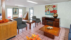 A spacious lobby with a wooden reception desk, two patterned armchairs, a coffee table with decorative items, a fireplace, and a large floral painting on the wall. - Red Carpet Inn - Louisville (Louisville)