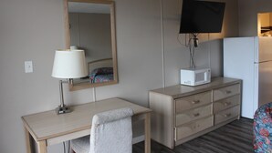 A hotel room with a desk, a chair, a dresser, a television mounted on the wall, and a microwave on the dresser. - Red Carpet Inn - Louisville (Louisville)