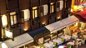 Un café al aire libre con mesas y sillas, un cartel que dice 'Acropolis Suites' y una calle adoquinada.