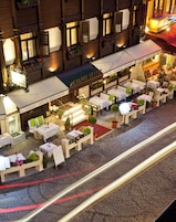 An outdoor café with tables and chairs, a sign for 'Acropolis Suites', and a cobblestone street.