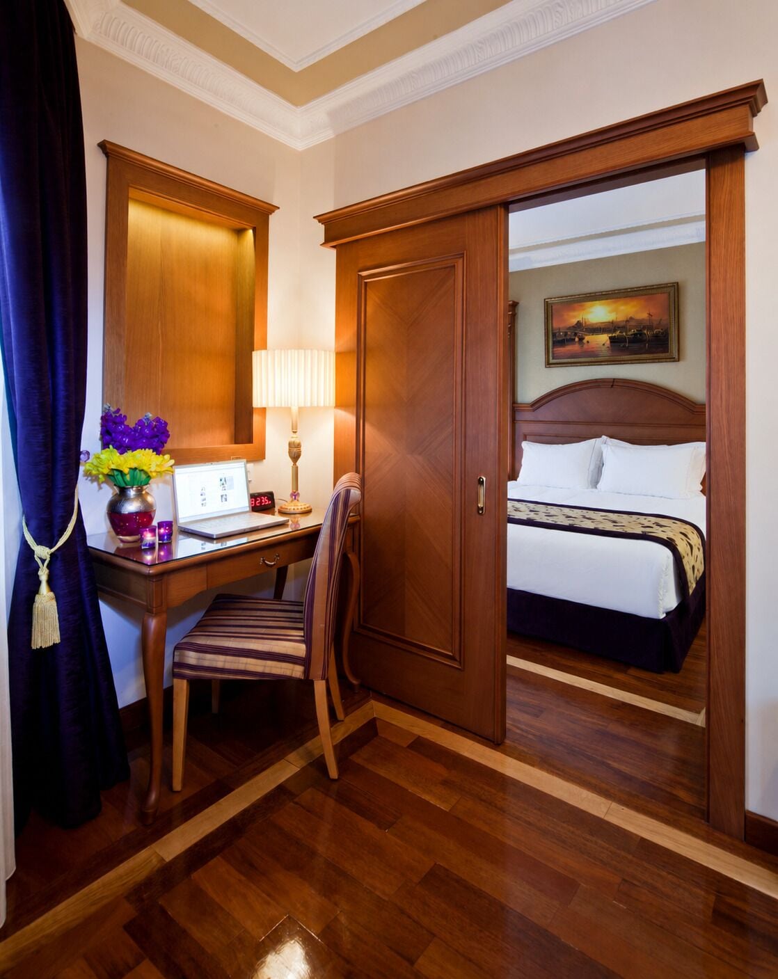 Une chambre d’hôtel avec un lit, un bureau avec une lampe, une chaise, une horloge et un tableau au mur.