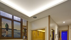 Una habitación moderna con un ventanal grande, una silla, una mesita con un florero y una estantería.