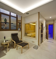 A modern room with a large window, a chair, a small table with a vase, and a bookshelf.