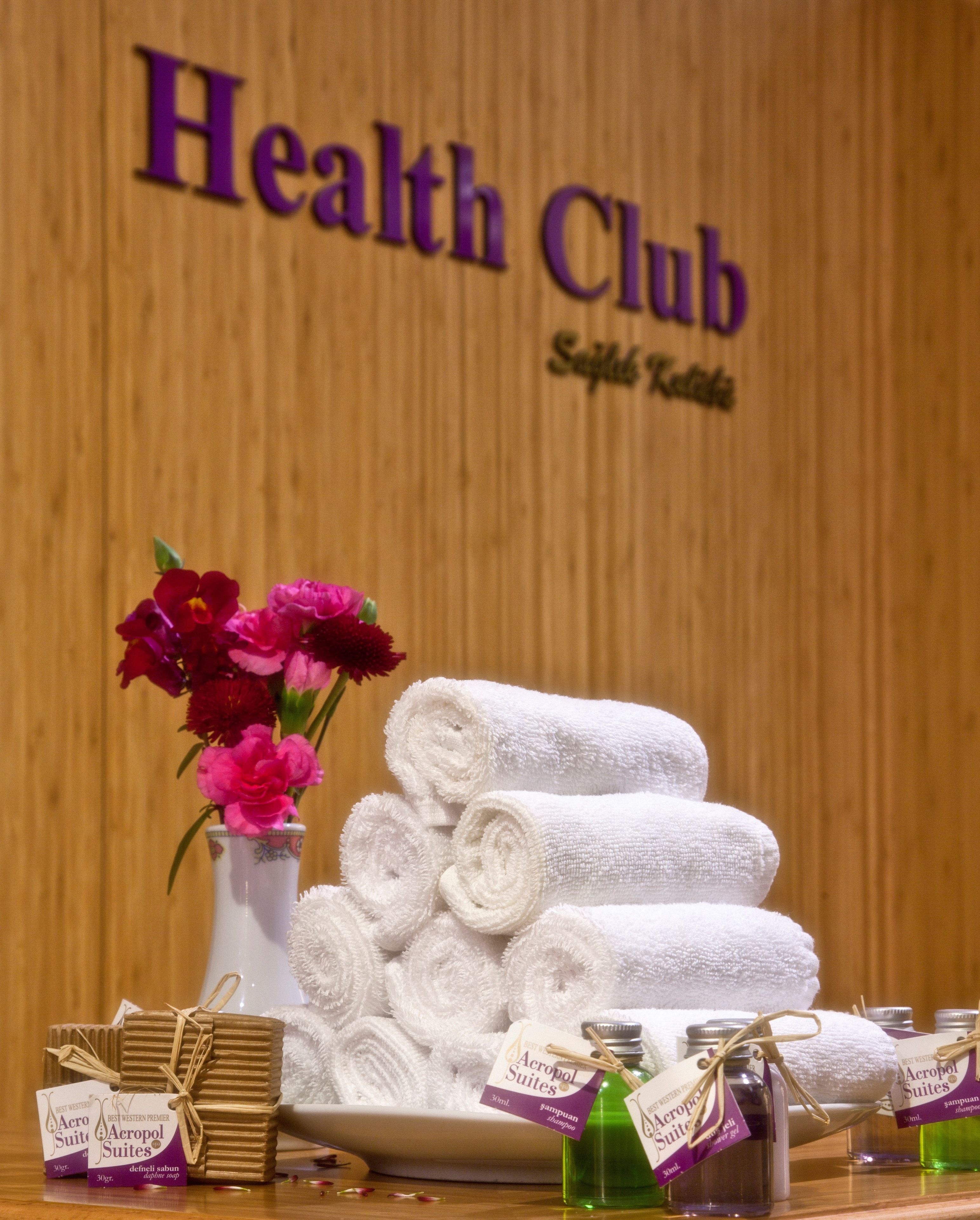 A display of white towels, a vase with pink flowers, and bottles of shampoo and conditioner at a Health Club.