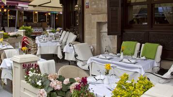 Un área de estar al aire libre del Café y Restaurante Jardín, con mesas dispuestas para comer, rodeada de sillas y arreglos florales.