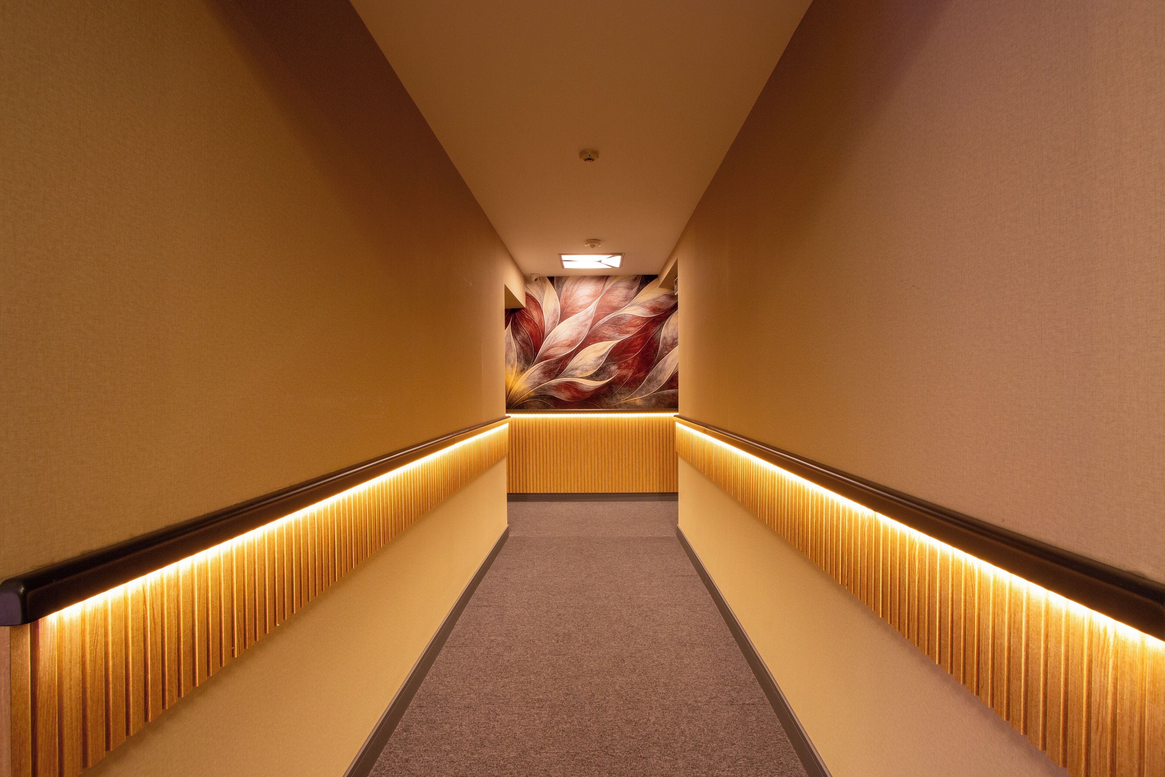 Ein Hotelgang mit Teppichboden, einer Wand mit Blättermuster und einer Lichtleiste entlang der Wände.