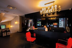 Zona de bar con diseño moderno, que incluye una barra negra, sillas rojas y un candelabro.