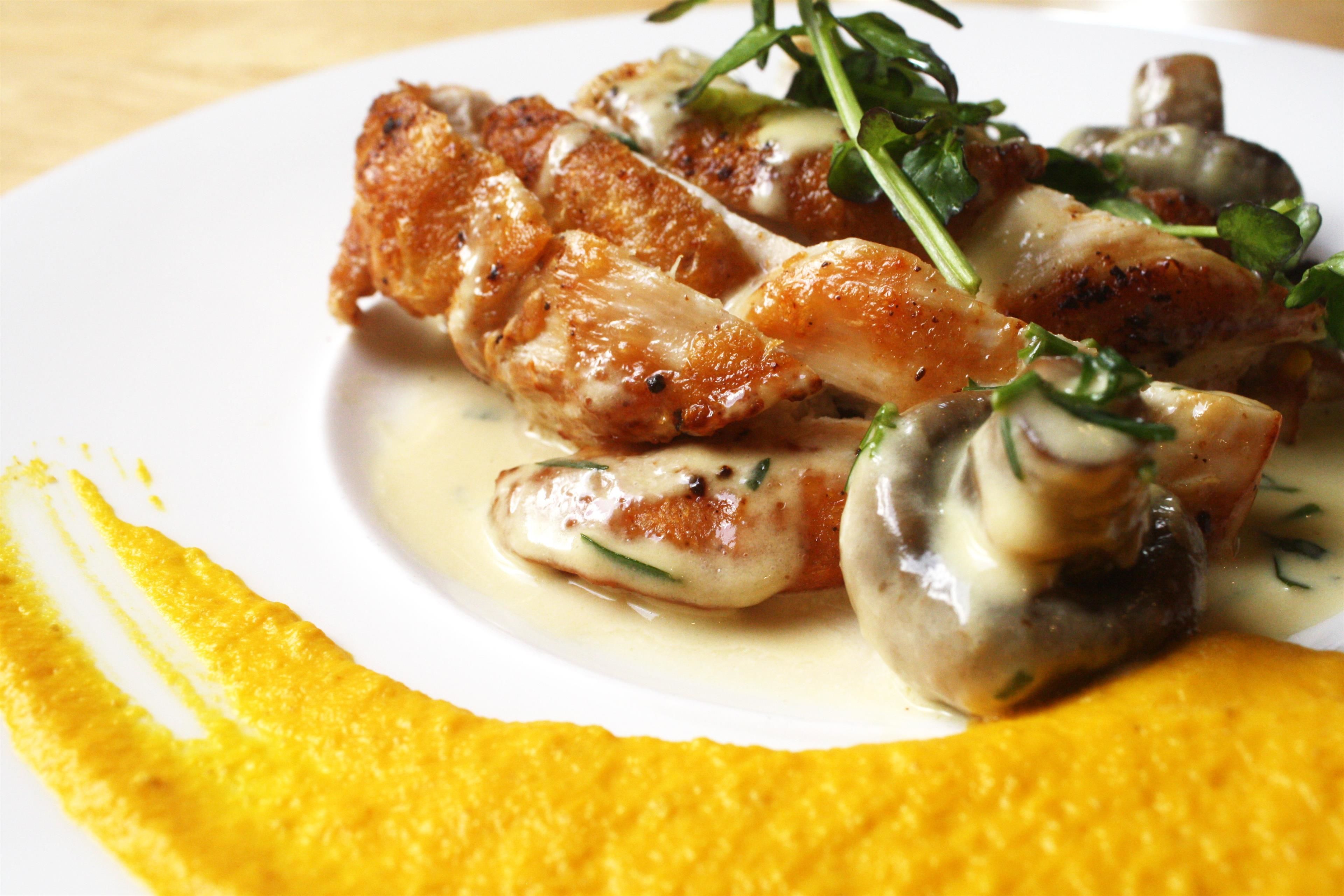 A plate of food with chicken, mushrooms, and greens, served on a white plate with a yellow garnish.