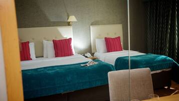 A hotel room with two beds, each with a teal bedspread and red striped pillows. There is a bedside table with a lamp and a telephone.