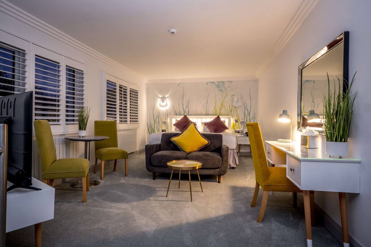 Une chambre d’hôtel moderne équipée d’un canapé, de deux fauteuils, d’un bureau et d’un grand miroir.