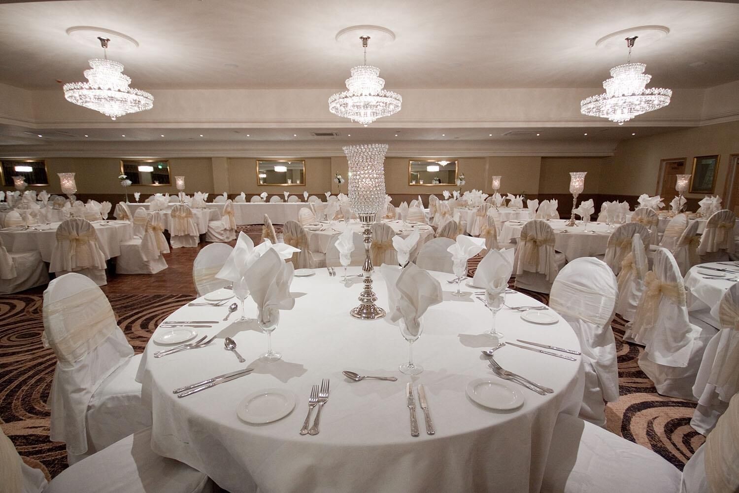 A banquet hall with round tables, white tablecloths, and crystal chandeliers.