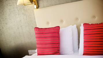 A neatly made bed with white and red striped pillows, a beige headboard, and a wall-mounted lamp.