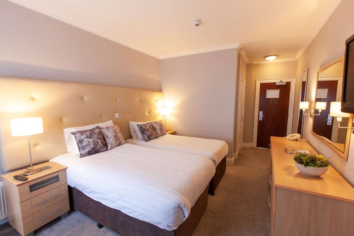 Une chambre d’hôtel avec un grand lit, des lampes de chevet, une commode en bois et un miroir.