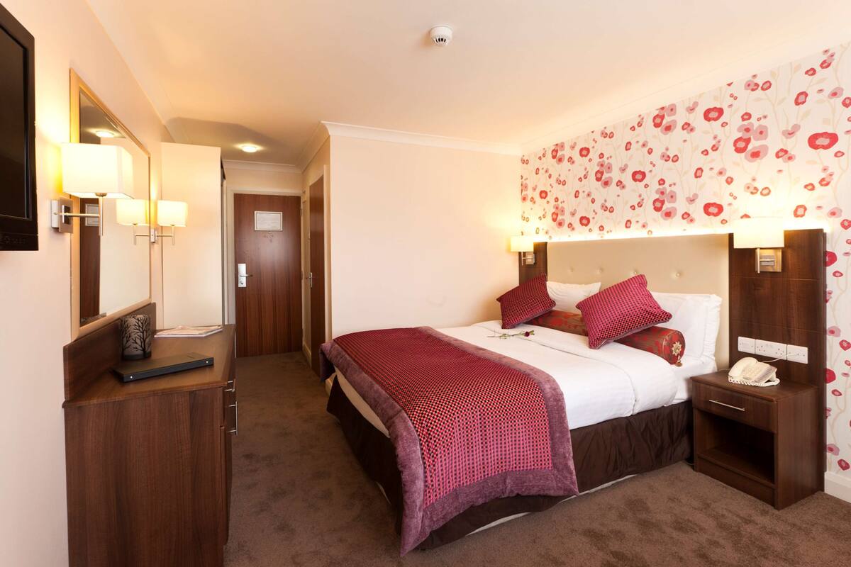 Une chambre d’hôtel avec un lit, des tables de chevet, un bureau et un miroir.