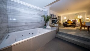 A modern bathroom with a large bathtub, a potted plant, and a staircase leading to a living area with a sofa and a dining table.