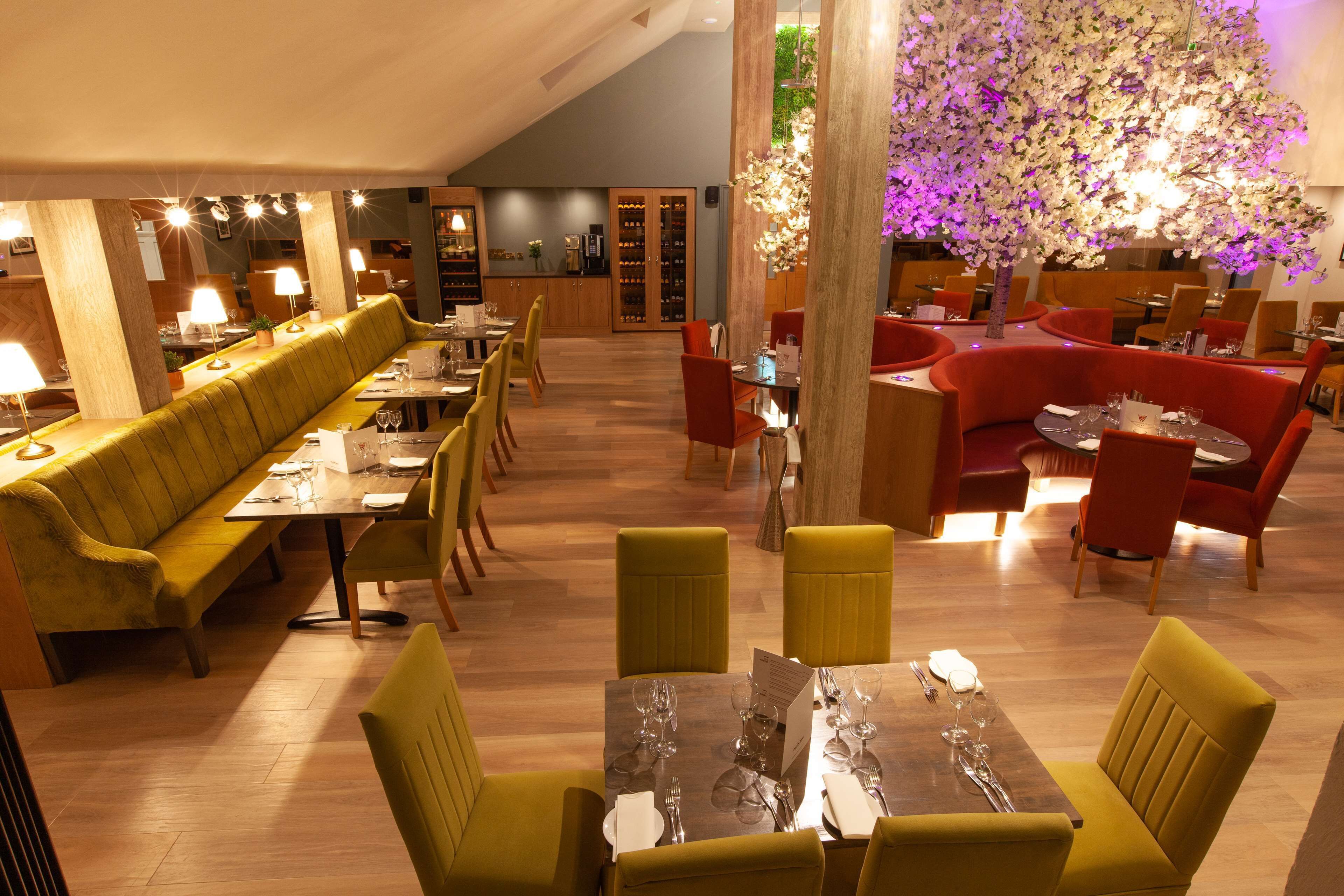 A restaurant with wooden flooring, yellow and red seating, and a large floral centerpiece.