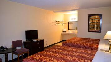 A hotel room with two beds, a desk with a chair, a television, and a bathroom with a sink and mirror.