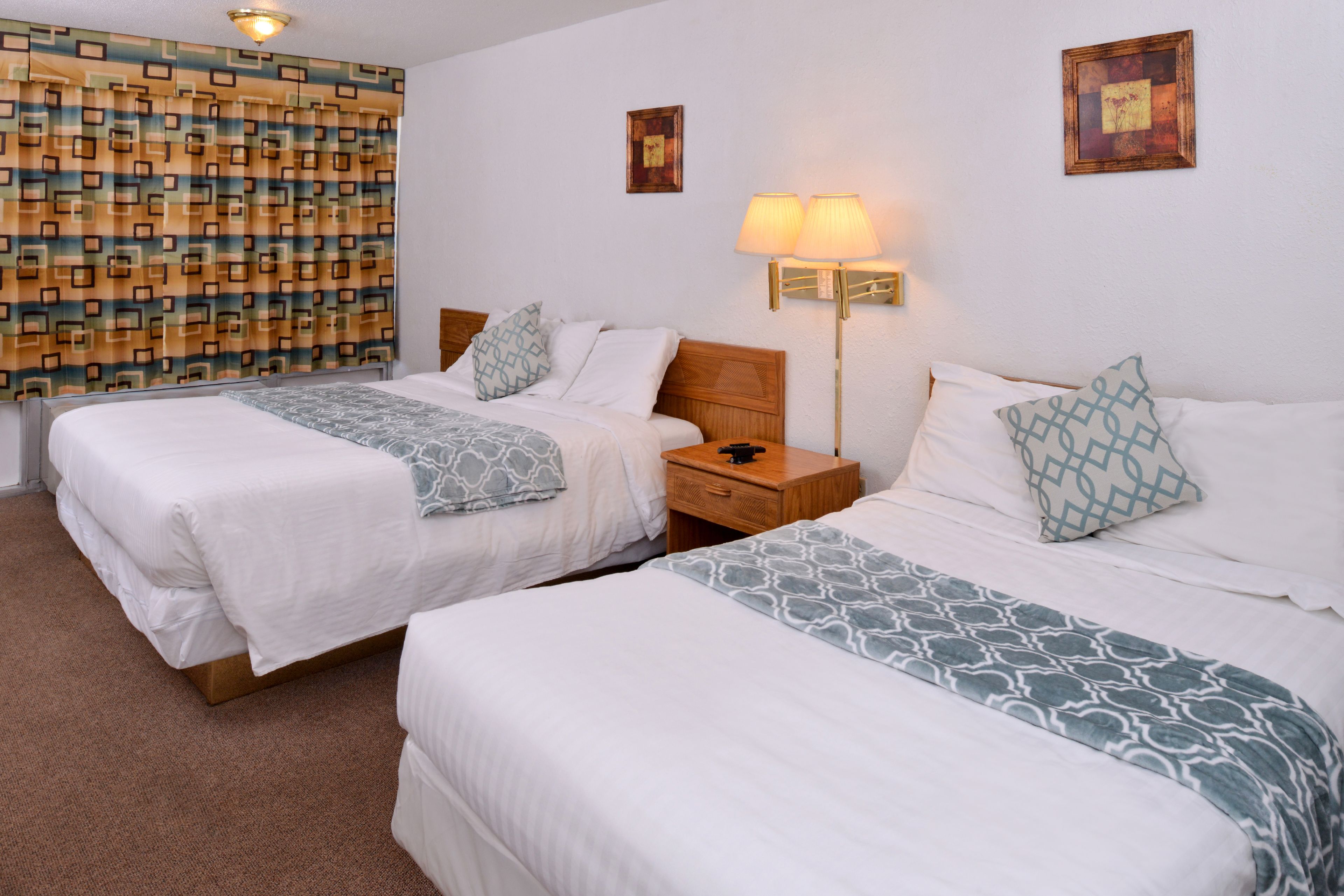 A hotel room with two beds, a nightstand, a lamp, and a patterned curtain.
