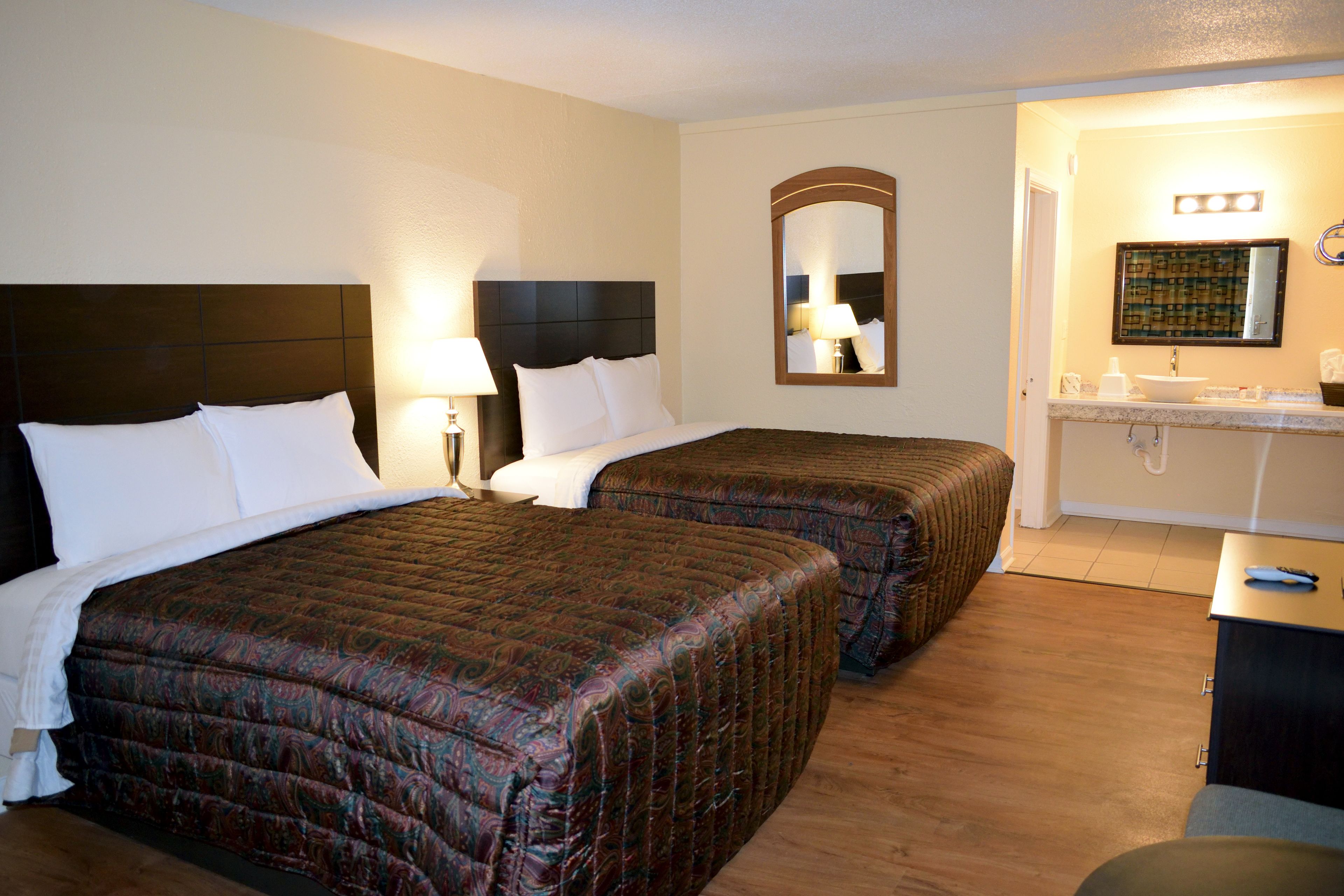 A hotel room with two beds, a bathroom with a sink and mirror, and a small table.