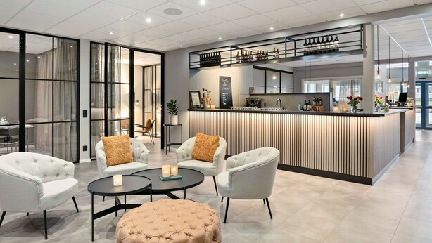 A modern hotel lobby with a reception desk, seating area, and a kitchen in the background. - Best Western Vrigstad Vardshus (Vrigstad)