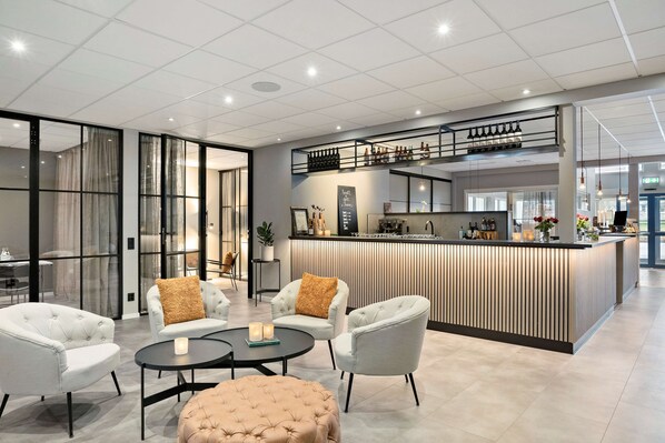 Experience a welcoming atmosphere in our stylish lobby, featuring a central reception desk, plush seating area, and a glimpse into the adjacent dining space.