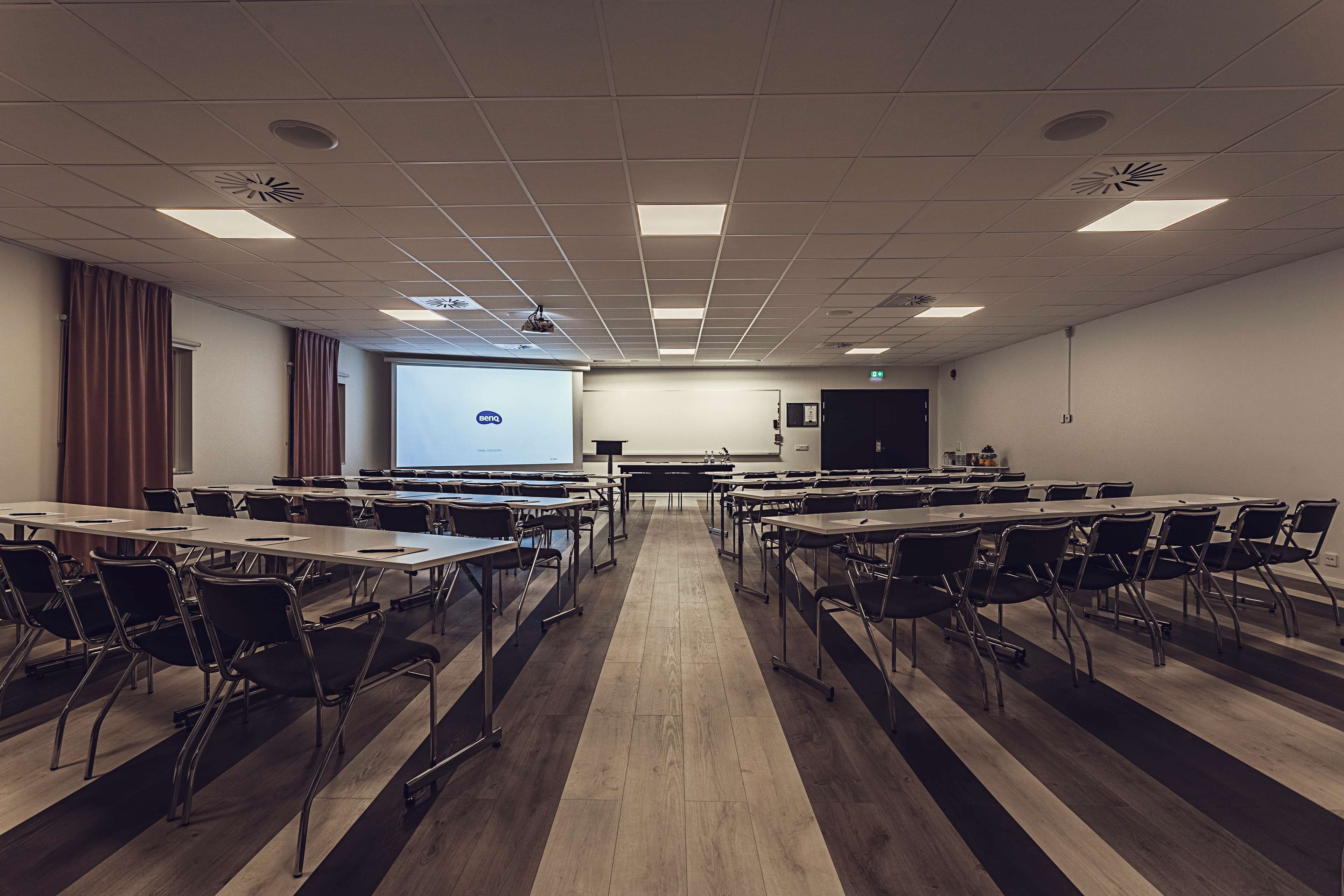 Una sala de conferències amb una taula llarga, cadires, una pantalla de projector i una pantalla de presentació.