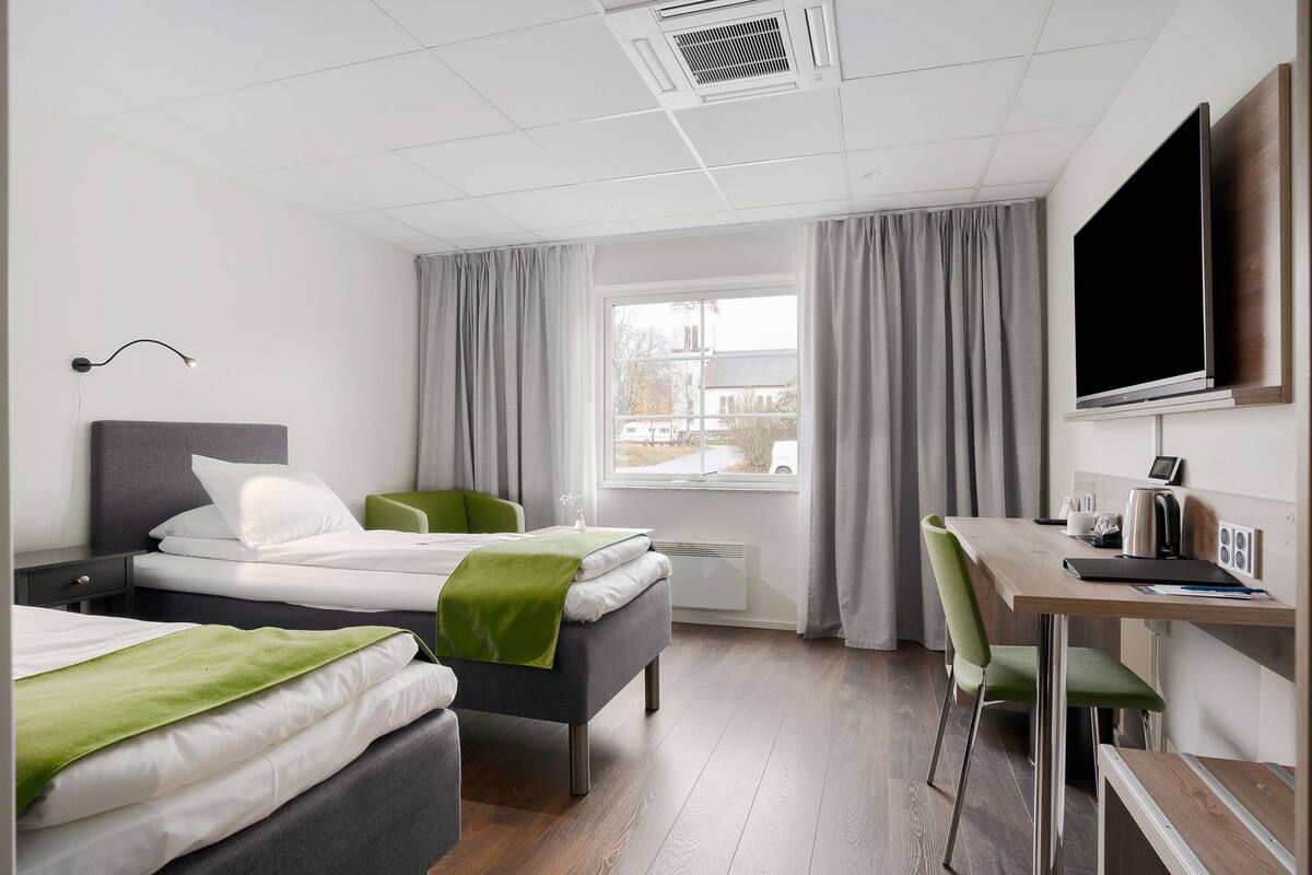 A modern hotel room with two beds, a desk with a computer, and a large TV.
