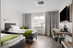 Two single beds with grey headboards and green throw blankets, a wooden desk, and a green chair.