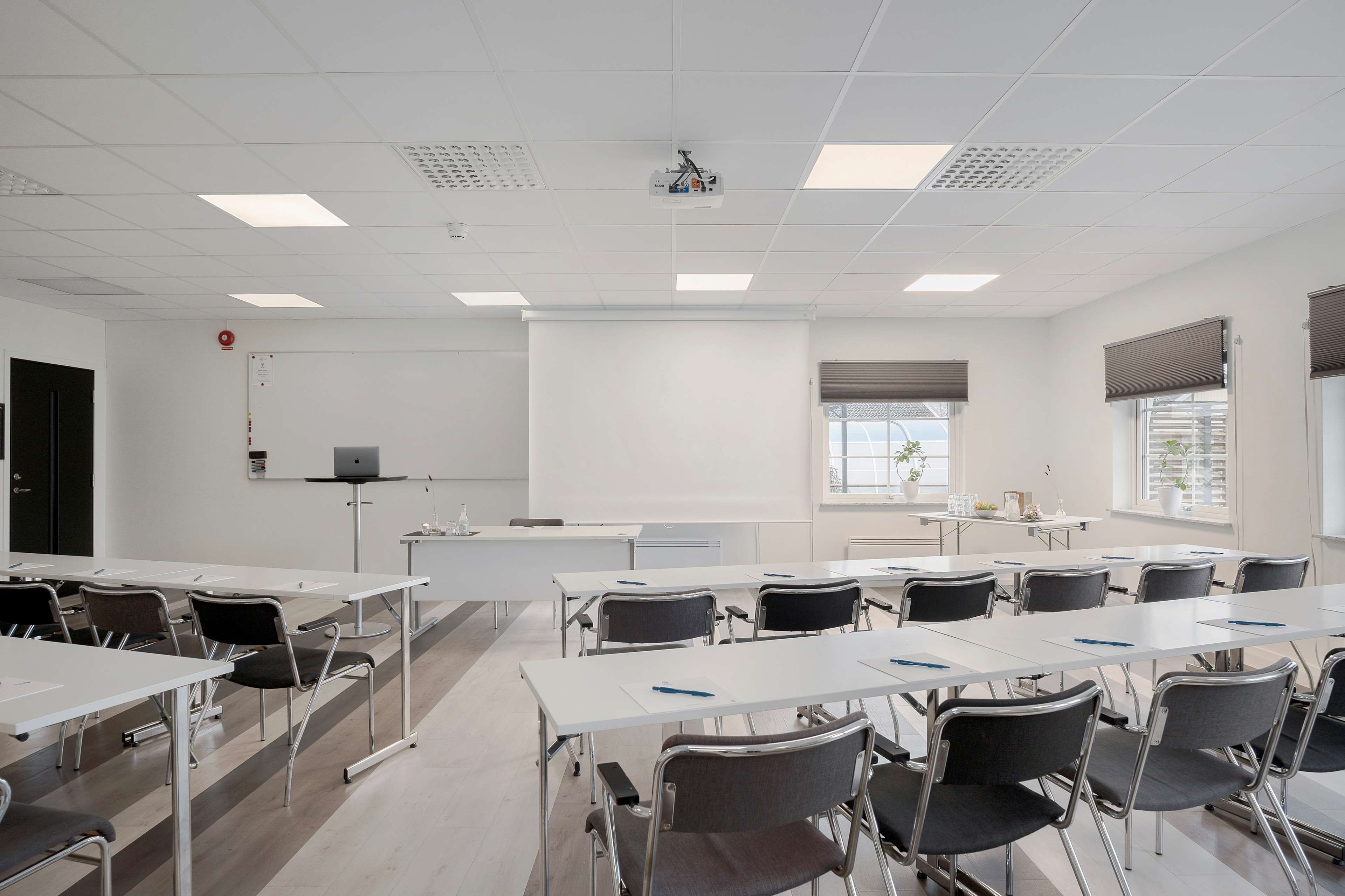 A conference room with white tables and chairs, a projector, and a whiteboard.
