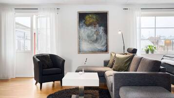 Una sala de estar moderna con una mesa de centro blanca, un sillón negro y un sofá gris. Un cuadro abstracto grande adorna la pared.