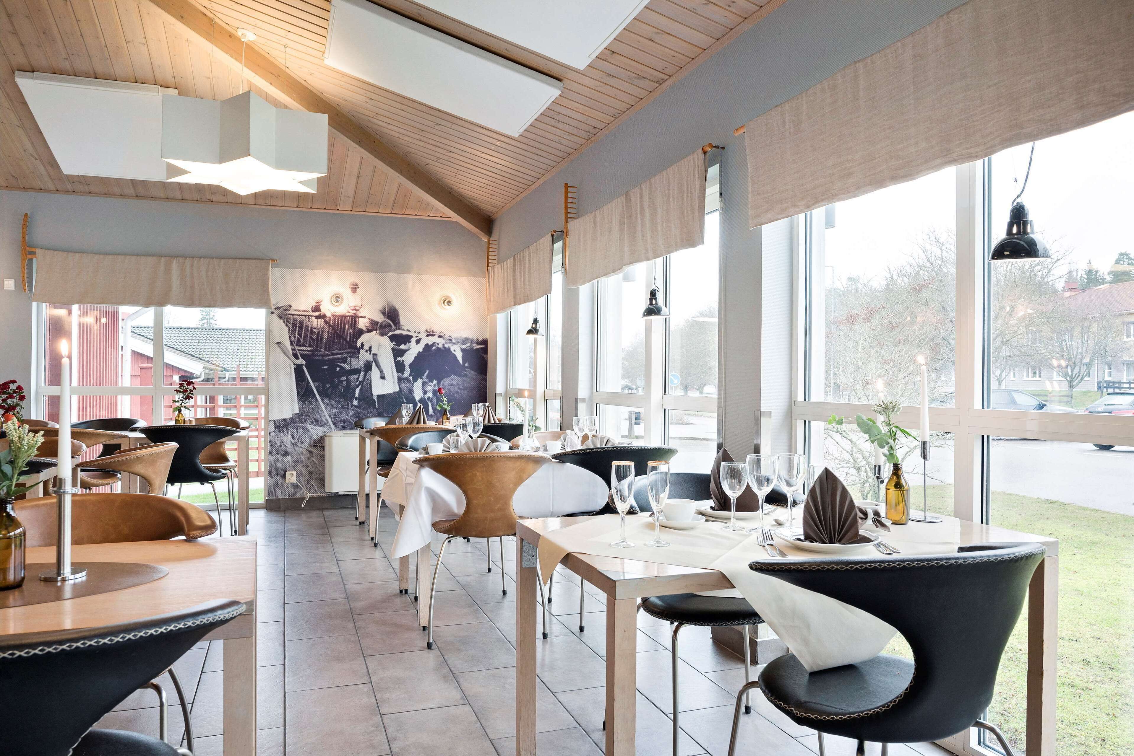En moderne restaurant med træbjælker i loftet, store vinduer og et muralmaleri på væggen.