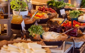 A variety of food items and condiments displayed on a table, including jars of jam, bowls of vegetables, and a dish with a yellow liquid.
