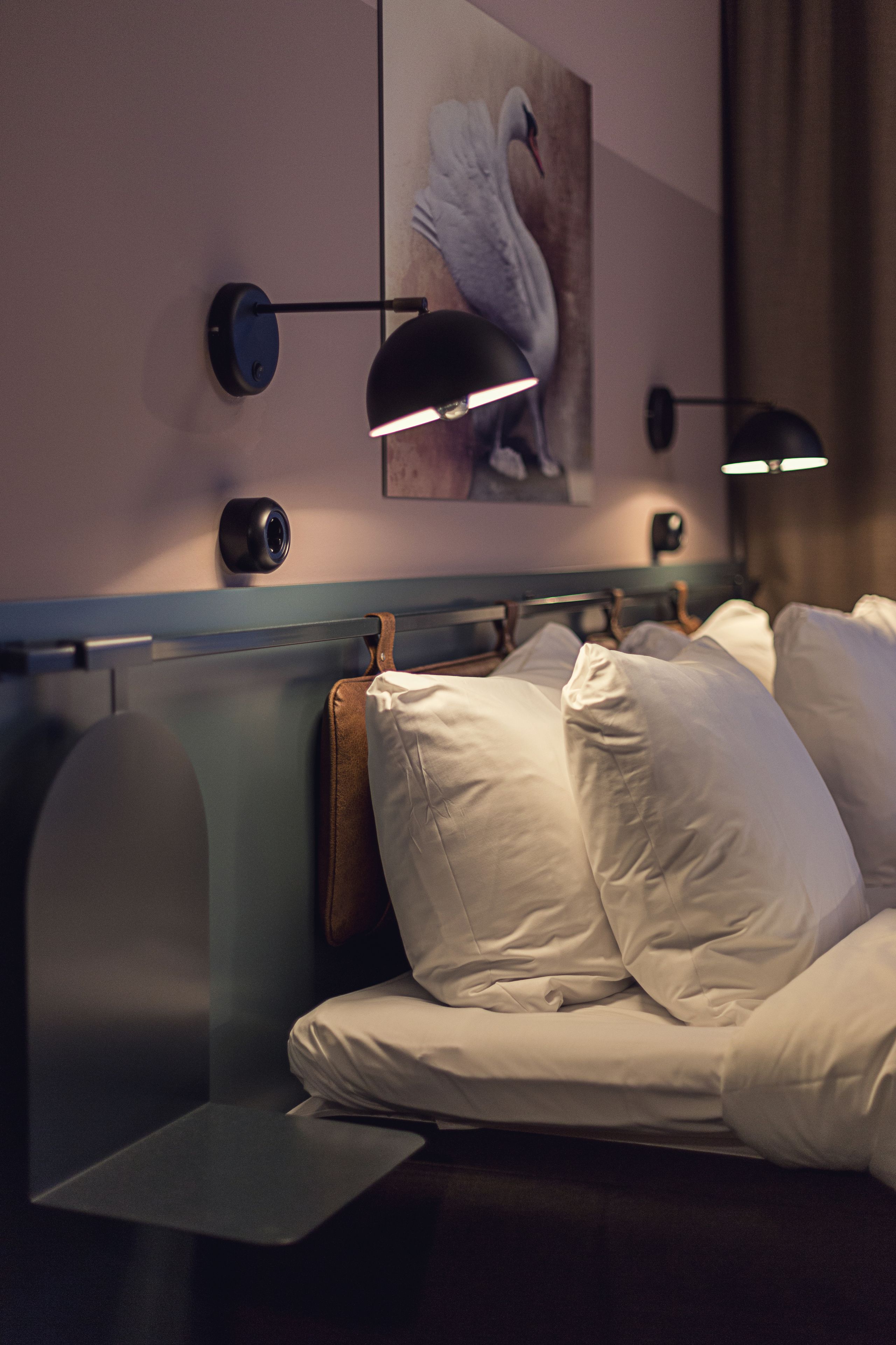 Habitació d'hotel moderna amb un llit, làmpades de nit, una càmera penjada a la paret i un quadre d'un cigne.