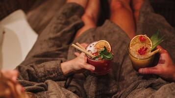 A person lying on a bed in a robe, holding a drink with a garnish.