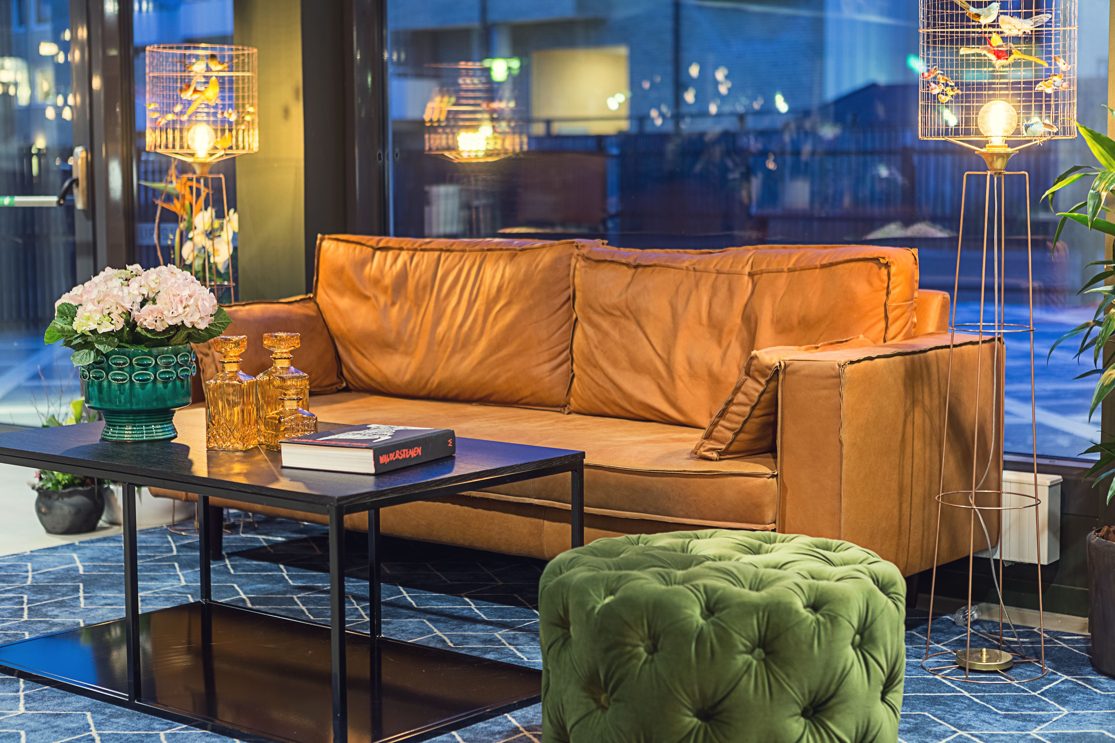 A modern living room with a leather sofa, a green ottoman, a coffee table, and a vase with flowers.