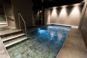 Una piscina interior con agua cristalina, una escalera metálica y paredes de azulejos.