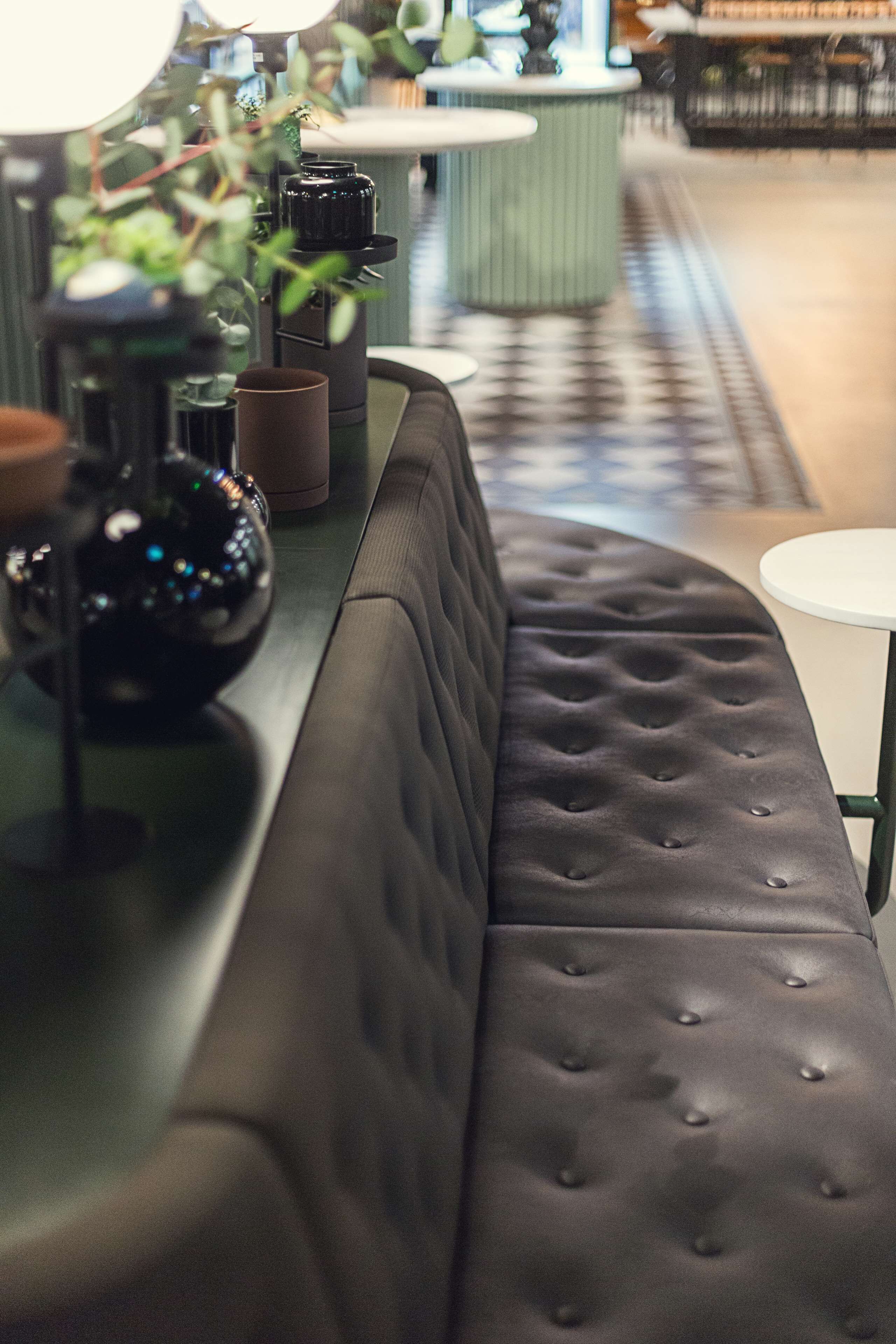 A modern bar area with a black cushioned bench, a green bar counter, and a white round table.