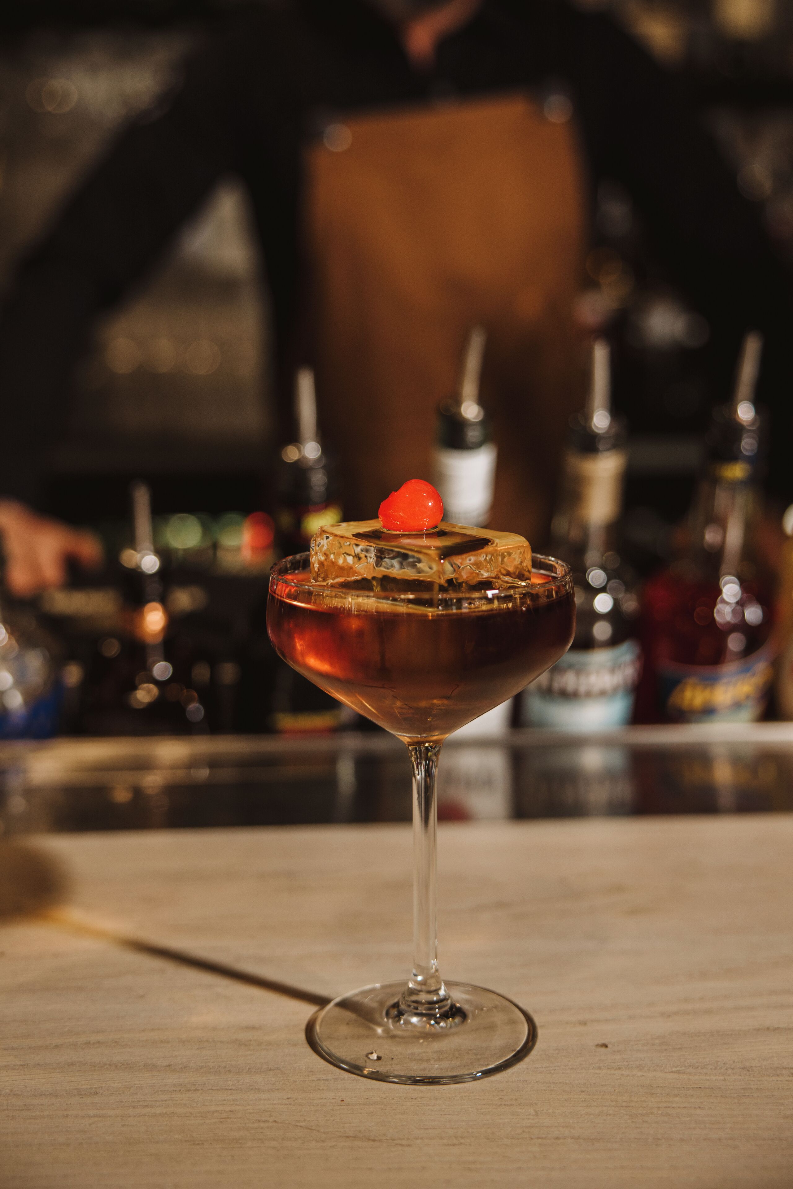Ein Cocktail im Stielglas mit einer Kirsche, Eiswürfeln und einem Orangenscheibchen am Rand.