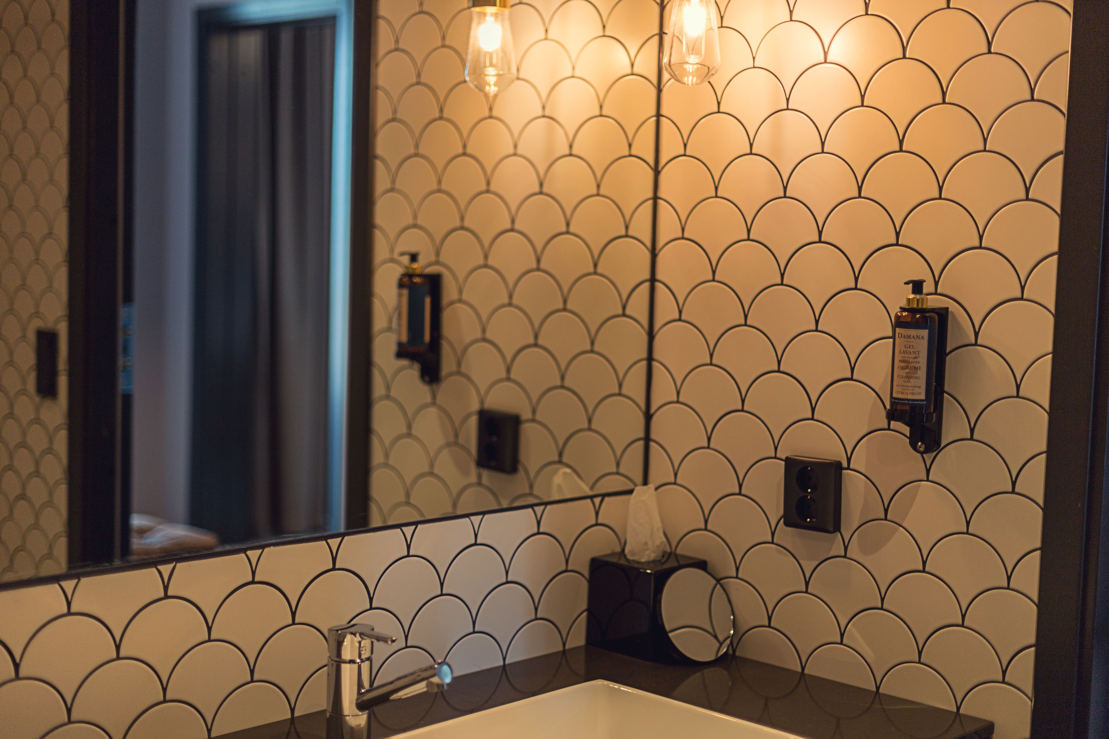 A bathroom with a tiled wall, a sink, and two wall-mounted lights.