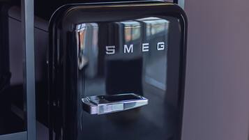 A black refrigerator with the brand name 'Smeg' on the front, placed on a wooden countertop.