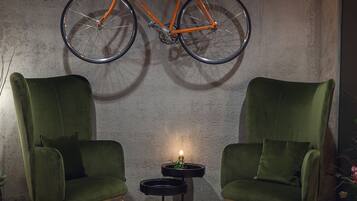 A room with two green armchairs, a small round table with a candle, and an orange bicycle hanging from the ceiling.