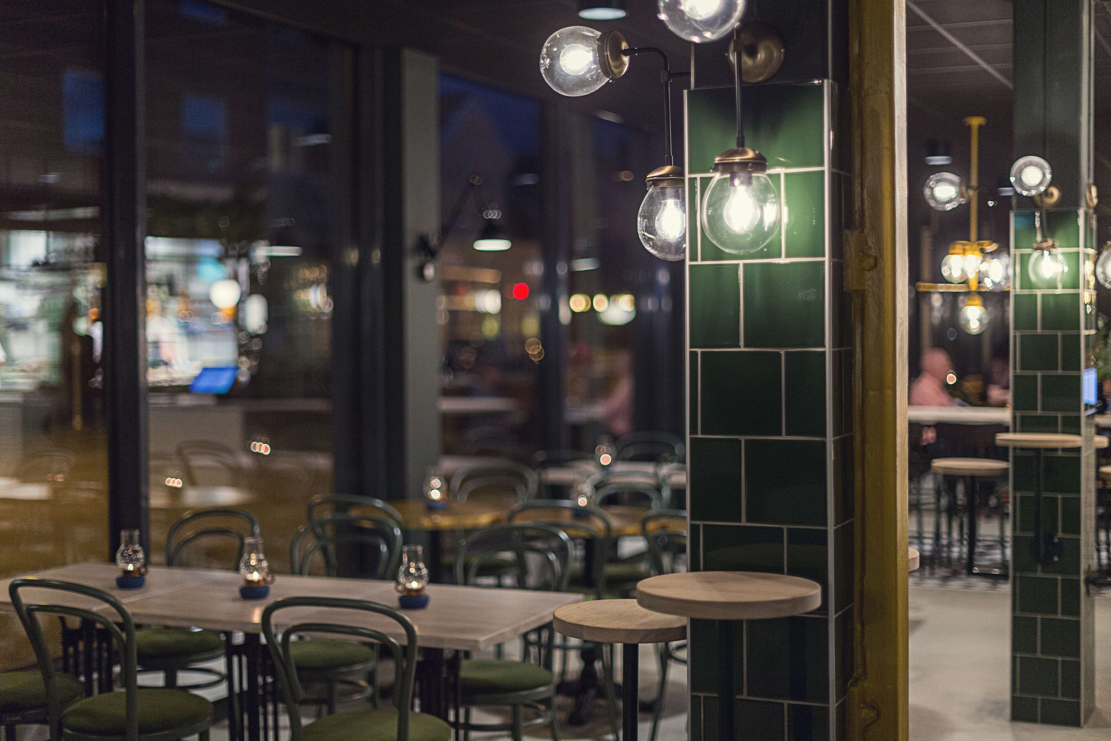 A restaurant interior with tables and chairs, hanging light fixtures, and a view of the street outside.