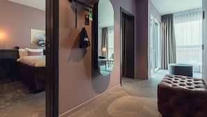 A modern hotel room with a large mirror, a bed, a seating area with a table and chairs, and a view of the city through large windows. - Best Western Plus Hus 57 (Angelholm)