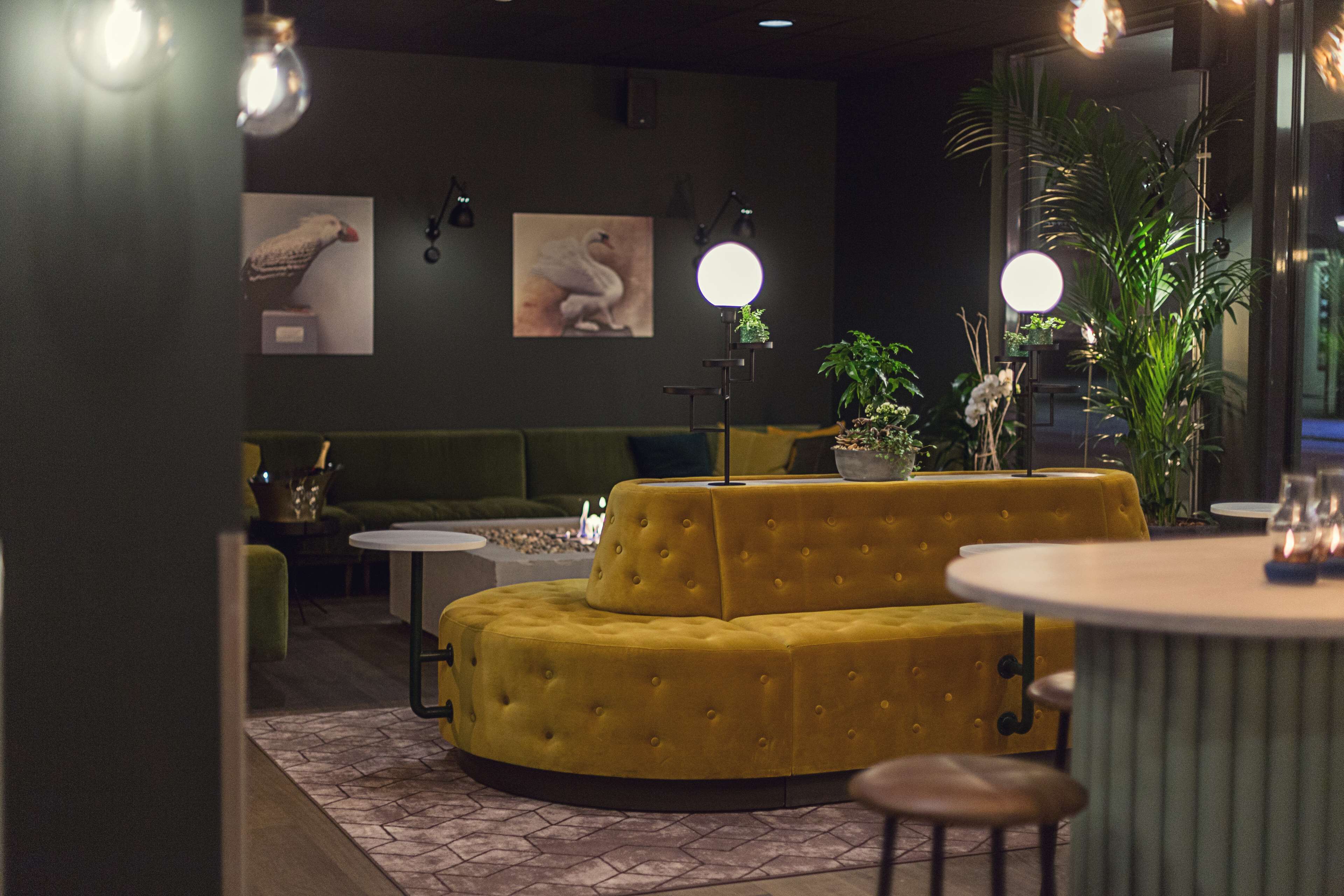 A modern interior with a yellow sofa, round tables, and green seating.