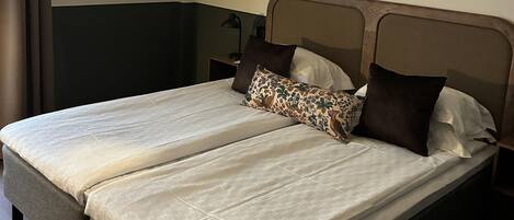 A double bed with two pillows, a bedside table, a lamp, and a hanging light fixture.
