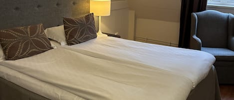A hotel room with a large bed, a chair, a lamp, and a window with curtains.