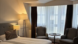 Una habitación de hotel con una cama grande, dos sillones, una mesita redonda y una lámpara.