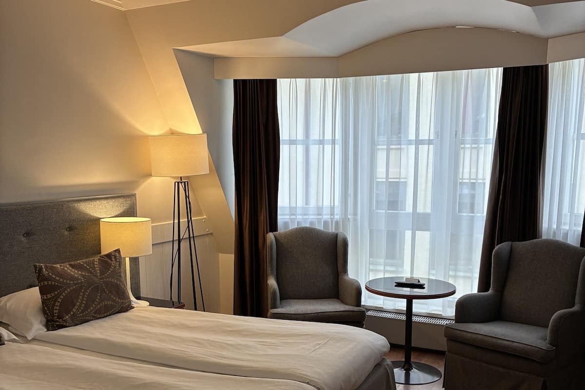 A hotel room with a large bed, two armchairs, a small round table, and a lamp.